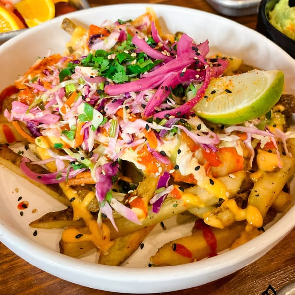 Nuri Fusion Street Kitchen's loaded fries topped with colorful slaw, sauces, sesame seeds, and a lime wedge.