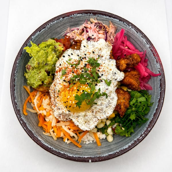 Colorful rice bowl with fried egg, guacamole, pickled onions, fried chicken, and vegetables.