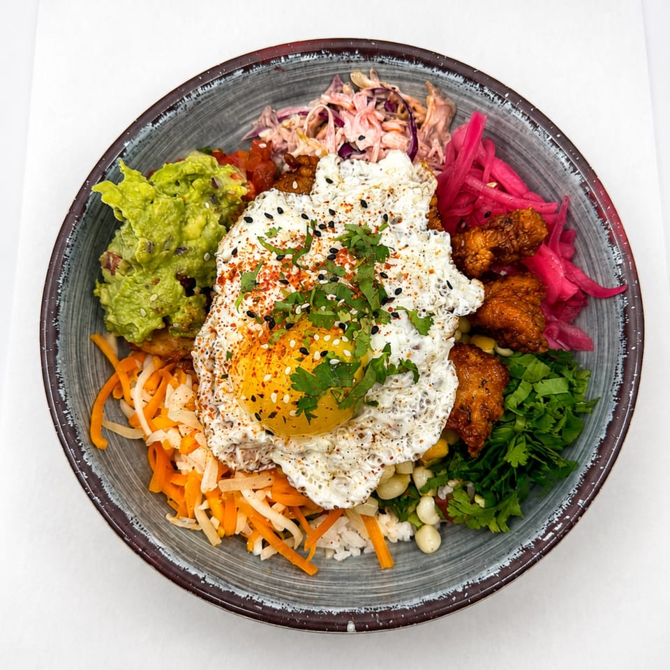 Colorful rice bowl with fried egg, guacamole, pickled onions, fried chicken, and vegetables.