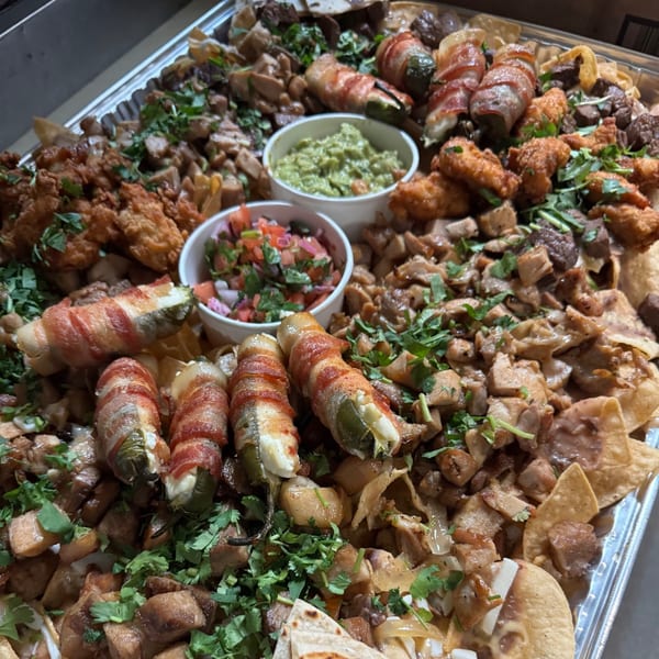 Large platter of nachos with various toppings, including bacon-wrapped jalapeños, chicken, and dips.