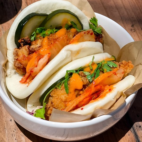 Three Nuri Fusion Street Kitchen bao buns with fried chicken, kimchi, and sauce in a white bowl.