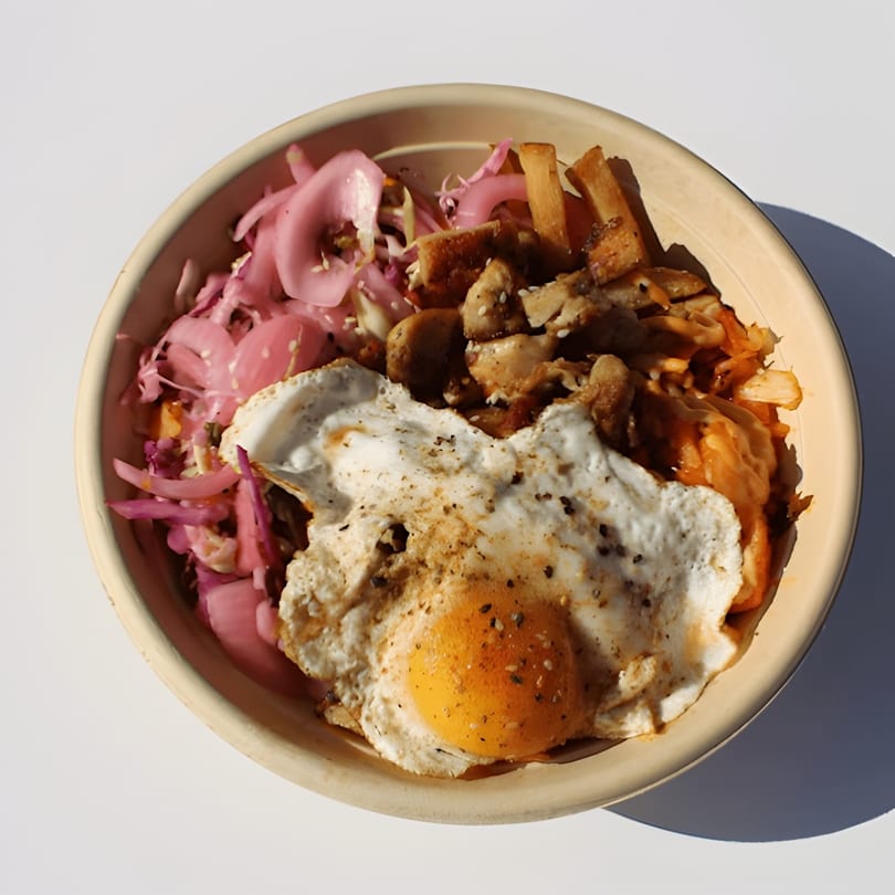 Disposable bowl with a fried egg, pickled red onions, seasoned chicken, and crispy fries.
